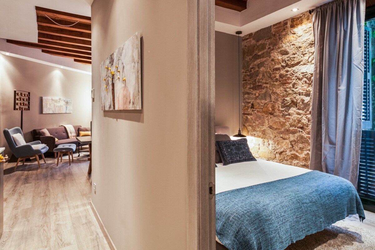 Ein modernes Schlafzimmer mit einer Steinwand, einem Bett mit blauer Decke und einer Sitzecke mit Sofa und Sesseln.