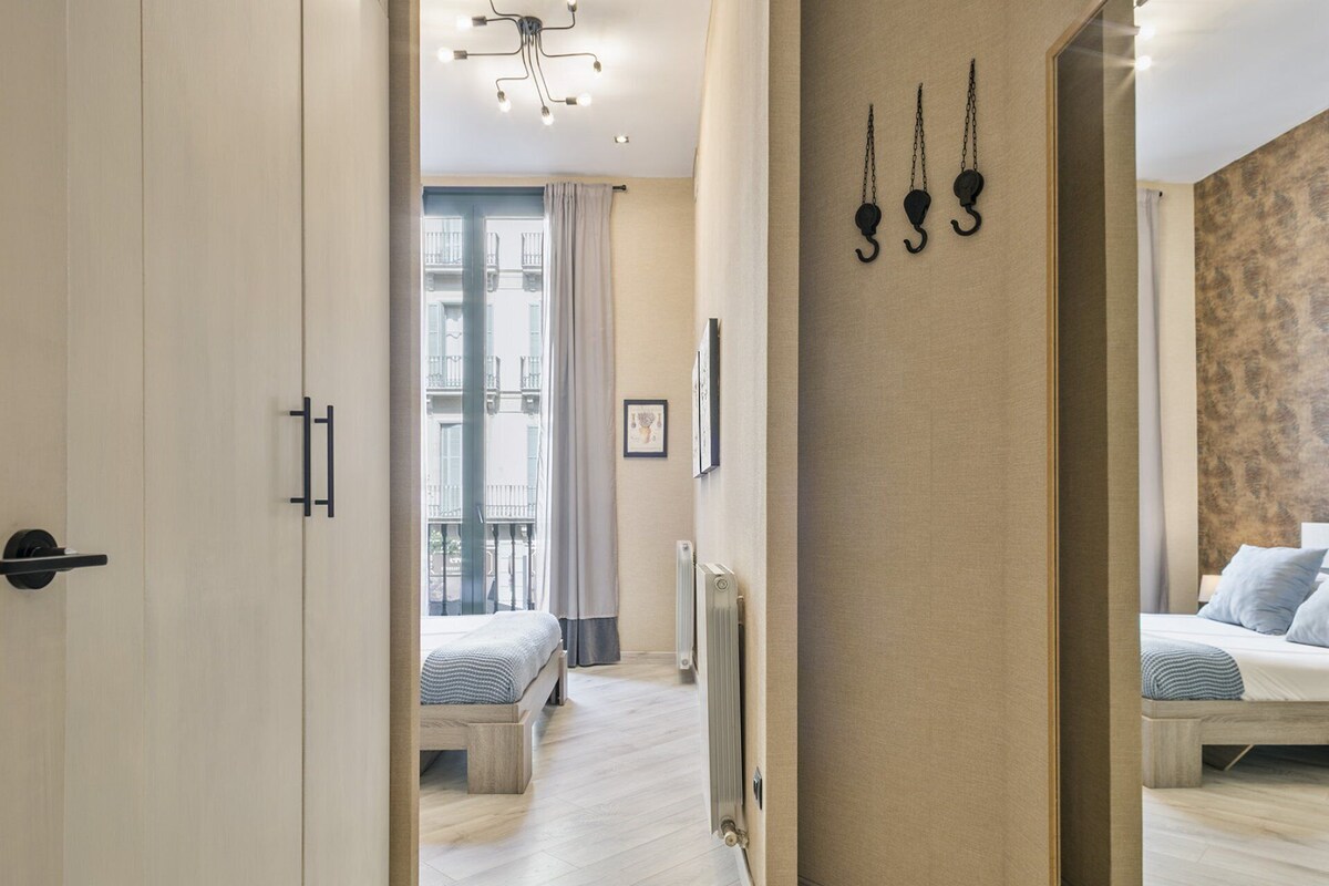 Ein Hotelzimmer mit einem Bett, einem Heizkörper, einem Fenster mit Vorhängen und einem zur nächsten Tür führenden Gang.