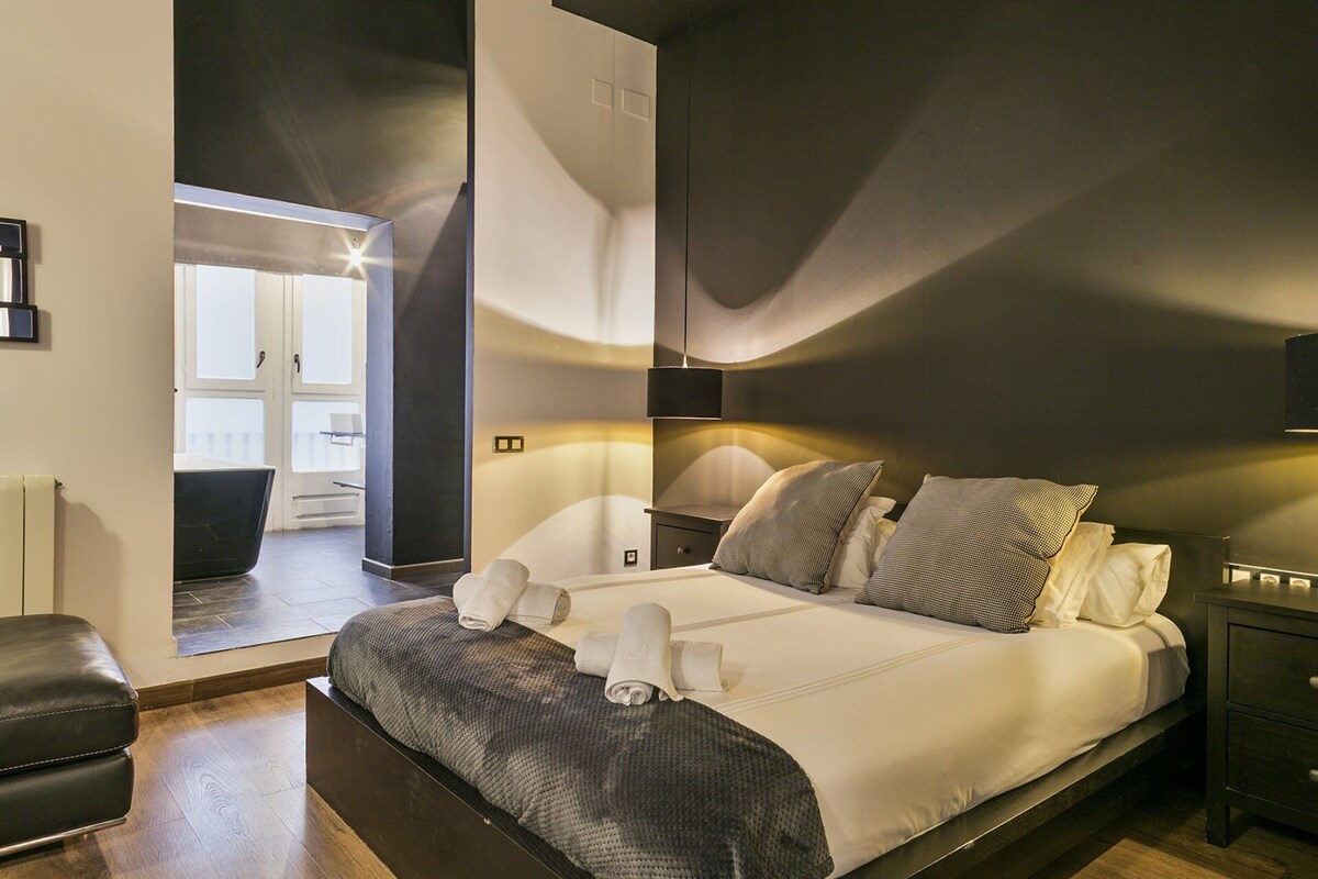 Ein modernes Schlafzimmer mit einem großen Bett, Nachttischen, einem Beistelltisch und Blick auf einen Balkon.