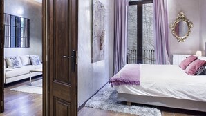 Ein Schlafzimmer mit einem Bett, einem Schlafsofa, einem großen Fenster mit Vorhängen, einem Spiegel und einer Tür.