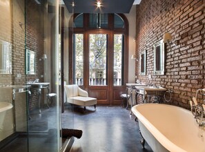 Ein modernes Badezimmer mit einer großen Badewanne, einer gläsernen Dusche und einem weißen Sessel.