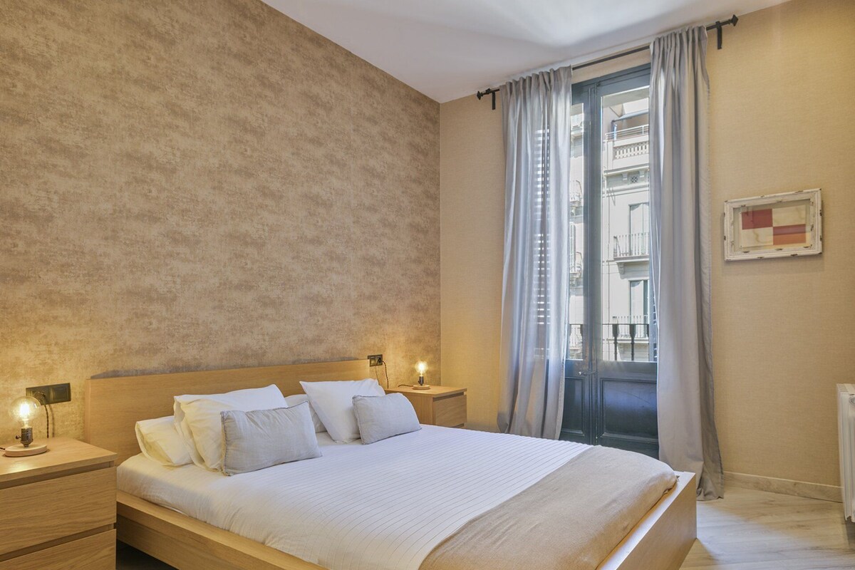Ein Schlafzimmer mit einem großen Bett, einem Holzkopfteil, zwei Nachttischen mit Lampen, einem Fenster mit Vorhängen und einer Heizung.