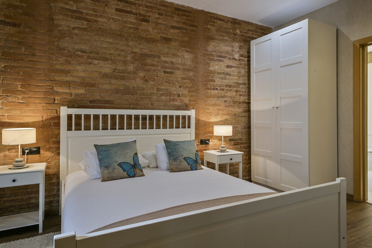 Ein Schlafzimmer mit Backsteinwand, einem weißen Bett mit zwei Kissen, zwei Nachttischen mit Lampen und einem Kleiderschrank.