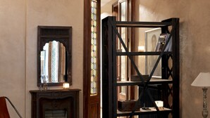 Ein Zimmer mit Kamin, Spiegel, Bücherregal und einer Tür zu einem anderen Raum.