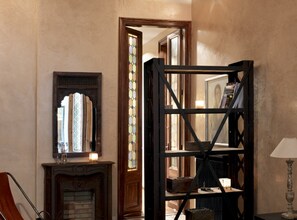 Ein Zimmer mit Kamin, Spiegel, Bücherregal und einer Tür zu einem anderen Raum.