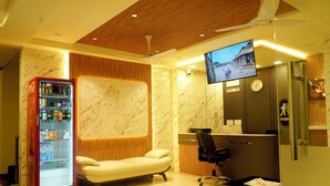 A hotel room with a sofa, a desk, a chair, a television, and a vending machine. - sithara inn by revtree (Hospet)
