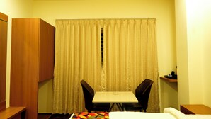 A hotel room with a bed, a desk, two chairs, a wardrobe, and a curtain. - sithara inn by revtree (Hospet)