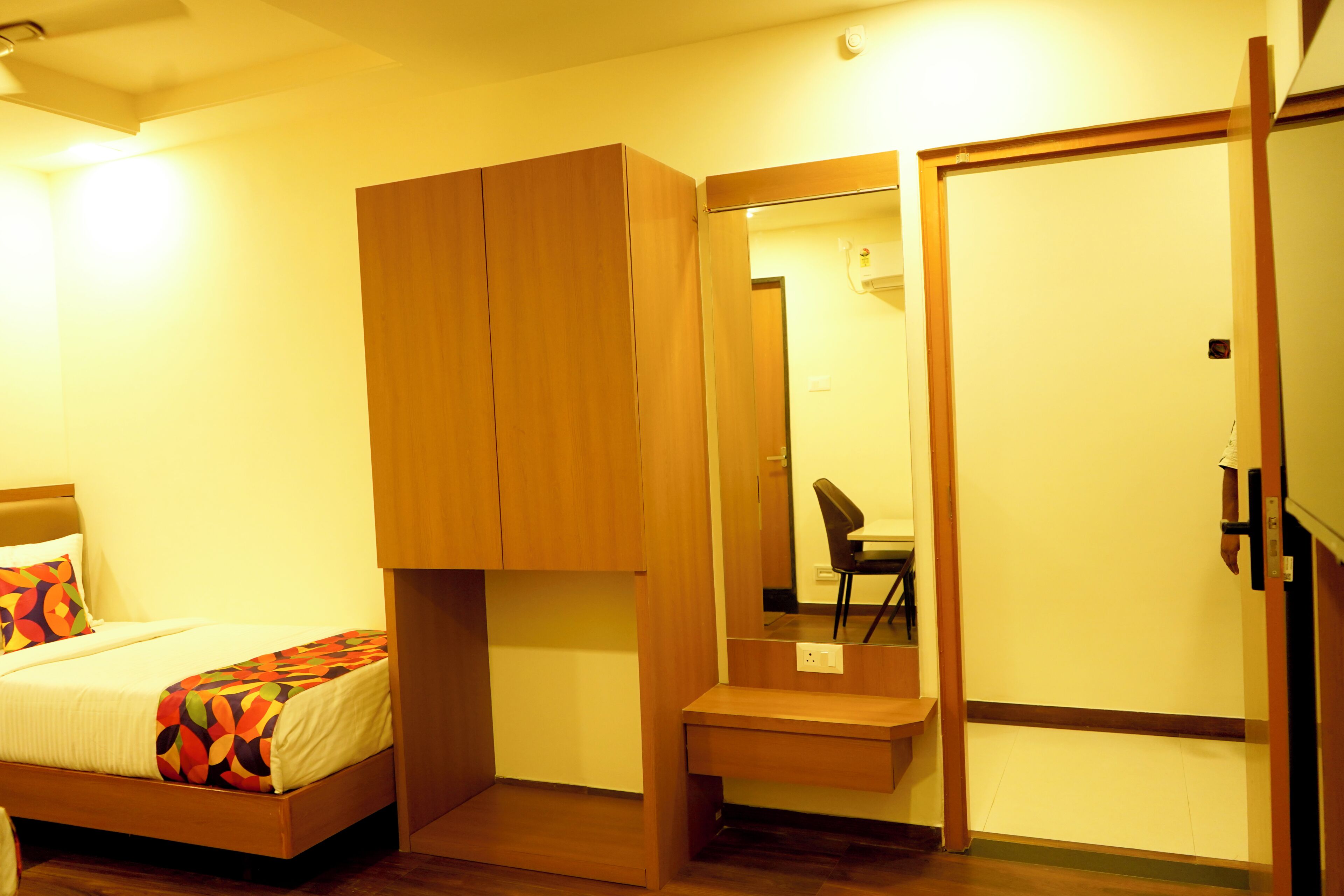 A bedroom with a bed, a wooden wardrobe, a mirror, and a small table.