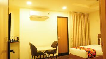 A hotel room with a bed, a desk with two chairs, an air conditioning unit, a door, and a curtain.