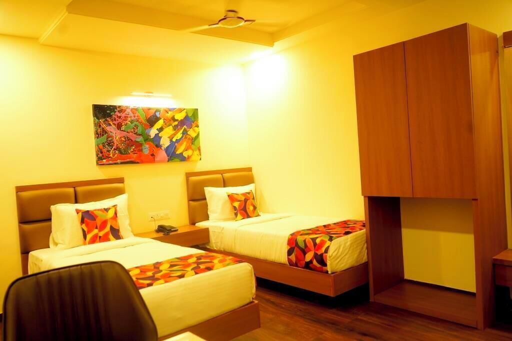 Habitación de hotel con dos camas, un armario de madera y un cuadro abstracto colorido en la pared.