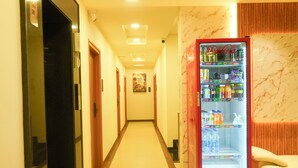 A hotel corridor with a vending machine stocked with beverages and a seating area with a white chair. - sithara inn by revtree (Hospet)