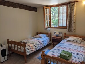 A bedroom with two wooden beds, a window with curtains, a bedside table with a lamp, and a small heater. - Charming gite with a private pool in the French countryside (Saint-Étienne-de-Fougères)