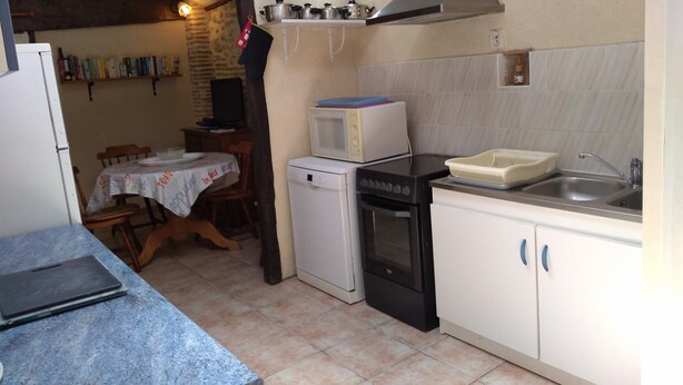 A compact kitchen with a microwave, oven, sink, and a dining area with a table and chairs. - Charming gite with a private pool in the French countryside (Saint-Étienne-de-Fougères)