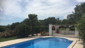 A swimming pool with a clear blue water surface, surrounded by a garden with various plants and flowers. - Charming gite with a private pool in the French countryside (Saint-Étienne-de-Fougères)