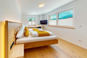 A modern bedroom with a wooden bed, a flat-screen TV, and a large window with a view. - Chalet AlpspitzBlick – Alpine Chalet with Sauna & Garden, Garmisch-Partenkirchen (Garmisch-Partenkirchen)