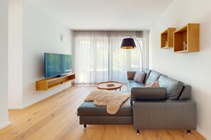 A modern living room with a sofa, a coffee table, a TV, and wooden shelves. - Chalet AlpspitzBlick – Alpine Chalet with Sauna & Garden, Garmisch-Partenkirchen (Garmisch-Partenkirchen)