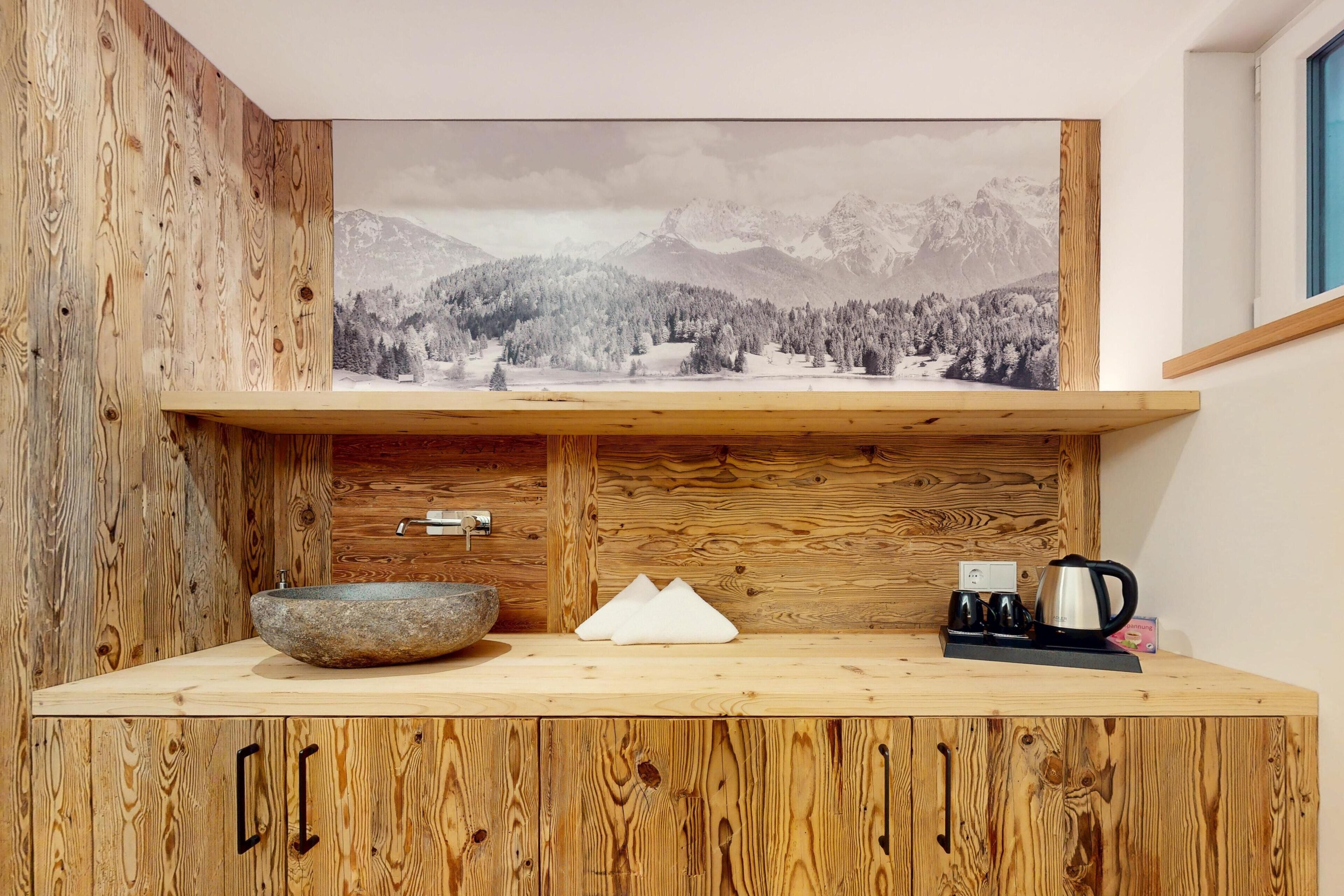 A wooden cabin interior with a rustic aesthetic, featuring a wooden cabinet with a large landscape painting, a stone bowl, a white object, and a coffee maker on the counter.