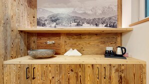Interior d'una cabana de fusta amb un estil rústic, amb un armari de fusta, un quadre de paisatge ampli, una safata de pedra, un objecte blanc i una cafetera al taulell.