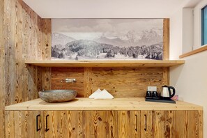 A wooden cabin interior with a rustic aesthetic, featuring a wooden cabinet with a large landscape painting, a stone bowl, a white object, and a coffee maker on the counter. - Chalet AlpspitzBlick – Alpine Chalet with Sauna & Garden, Garmisch-Partenkirchen (Garmisch-Partenkirchen)