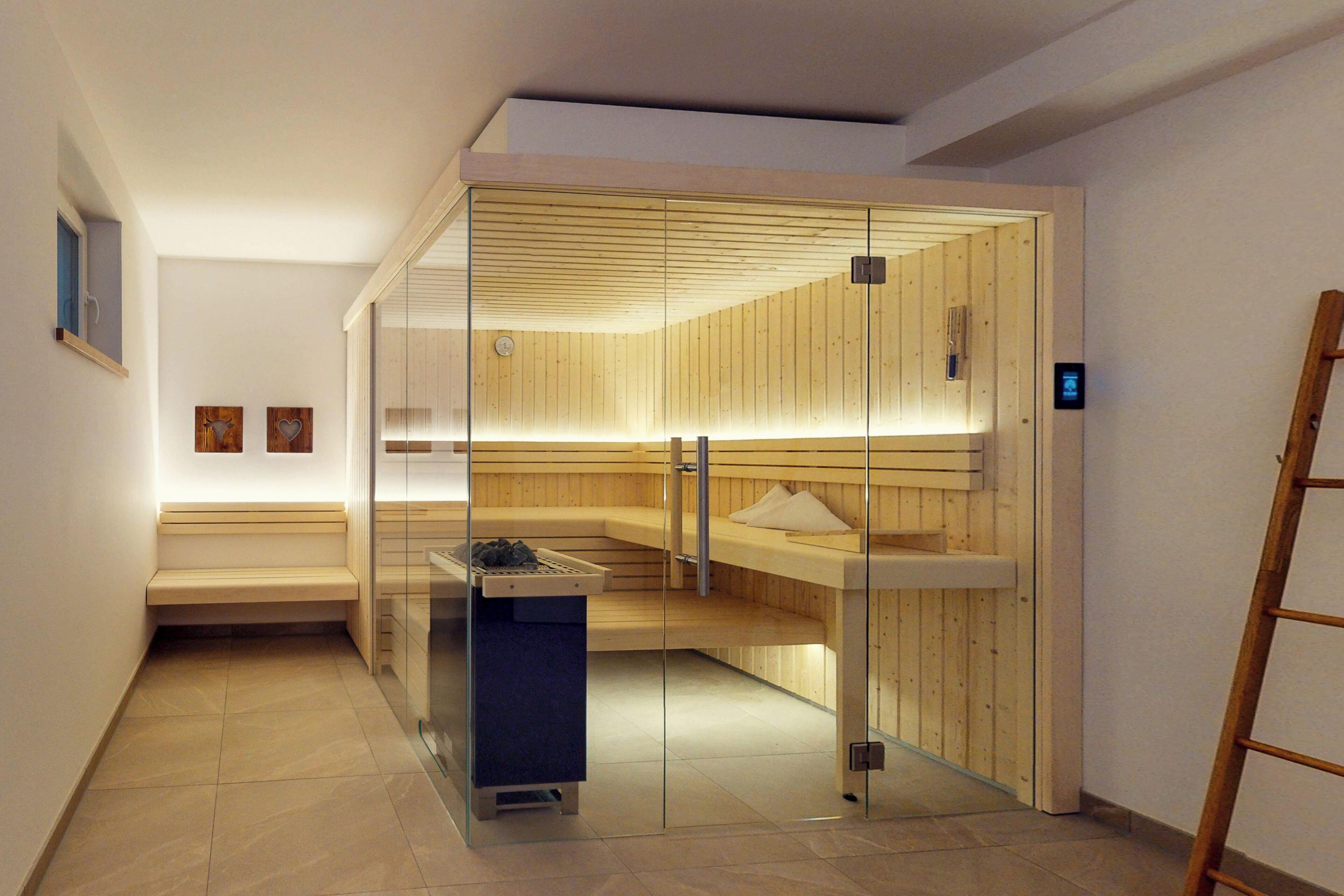 A sauna room with a glass partition, wooden benches, and a bench with a towel.