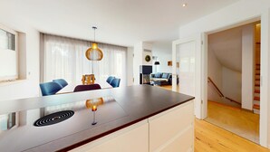 Una cuina moderna amb una illa central, zona de menjador amb cadires blaves i una escala que condueix a un altre nivell.
