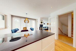 A modern kitchen with a central island, dining area with blue chairs, and a staircase leading to another level. - Chalet AlpspitzBlick – Alpine Chalet with Sauna & Garden, Garmisch-Partenkirchen (Garmisch-Partenkirchen)