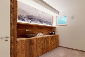 Un meuble en bois avec un évier, une fenêtre et un tableau représentant un paysage de montagne.
