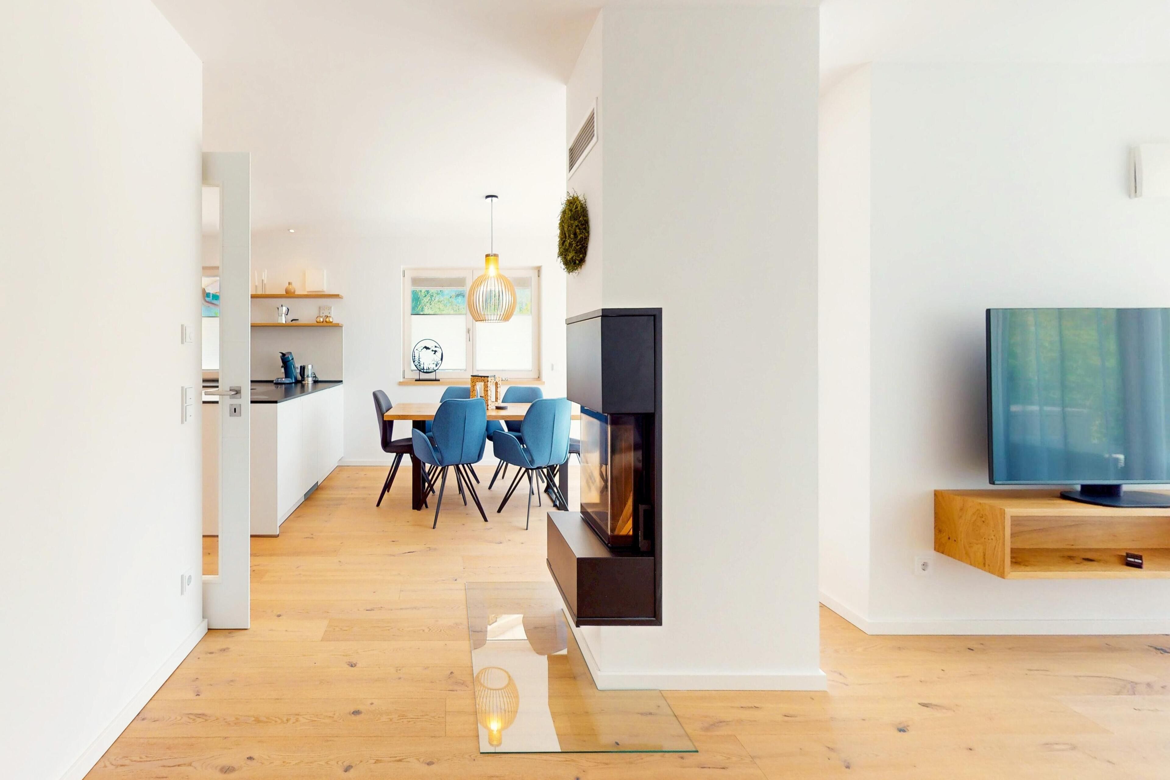 A modern living room with a TV, a fireplace, and a dining area with chairs and a table.
