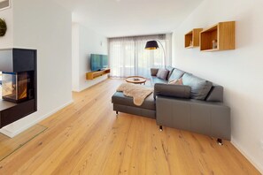 A modern living room with a sectional sofa, a flat-screen TV, wooden flooring, and built-in shelves. - Chalet AlpspitzBlick – Alpine Chalet with Sauna & Garden, Garmisch-Partenkirchen (Garmisch-Partenkirchen)