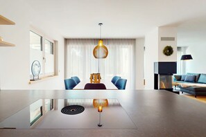 A modern living room with a dining area, featuring a central table, blue chairs, a sofa, and a hanging light fixture. - Chalet AlpspitzBlick – Alpine Chalet with Sauna & Garden, Garmisch-Partenkirchen (Garmisch-Partenkirchen)