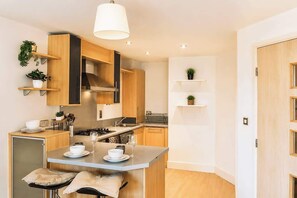 A modern kitchen with wooden cabinets, a central island, and built-in shelves. - Modern Brindley Point Apt, Near Canals & Broad (West Midlands)