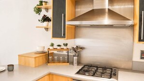 Moderni keittiö, jossa on ruostumattomasta teräksestä valmistetut kodinkoneet, puukaapit ja sisäänrakennettu liesi.