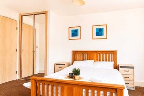 A bedroom with a wooden bed, a nightstand, a bedside table, and a wardrobe. - Modern Brindley Point Apt, Near Canals & Broad (West Midlands)