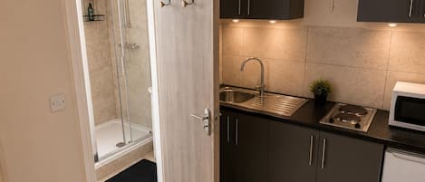 A compact kitchen with a built-in microwave, a sink, and a shower area.