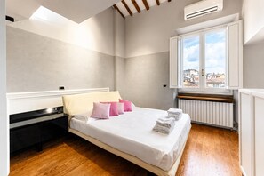 Ein Schlafzimmer mit Bett, Kissen, Heizkörper und einem Fenster mit Blick auf Gebäude.