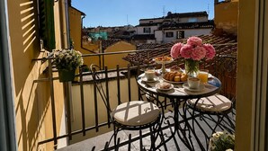 A balcony with a table set for breakfast, a potted plant, and a view of the cityscape. - Vigna Luxury Florence (Firenze)