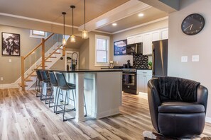 A modern kitchen with a central island, bar stools, a refrigerator, and a clock on the wall. - 300 Feet from Outlaw Square. 9 Shine is the best vacation rental in Deadwood. (Deadwood)