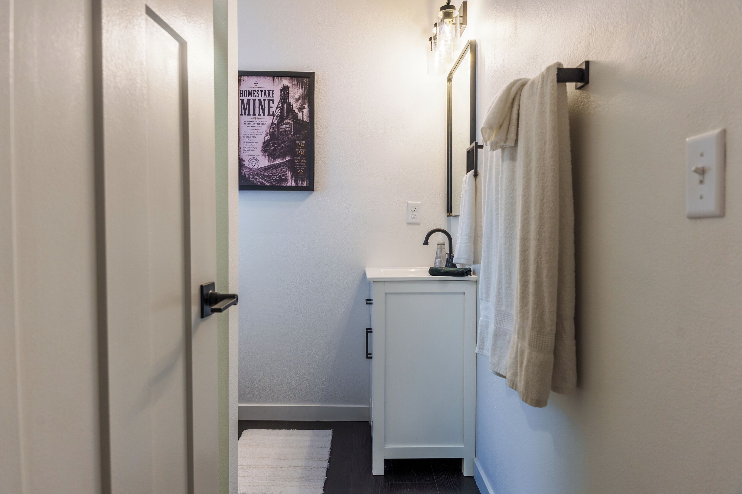 Un baño con un lavabo blanco, un perchero y un cartel en la pared.