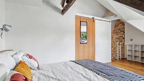 Un dormitorio con cama, almohadas, una lámpara, una puerta de madera y una pared de piedra.