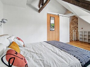 A bedroom with a bed, pillows, a lamp, a wooden door, and a stone wall. - Charming two-story apartment in the heart of Pont-Aven (Pont-Aven)