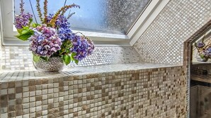 Un baño con salpicadero de azulejos y una ventana con un arreglo floral.
