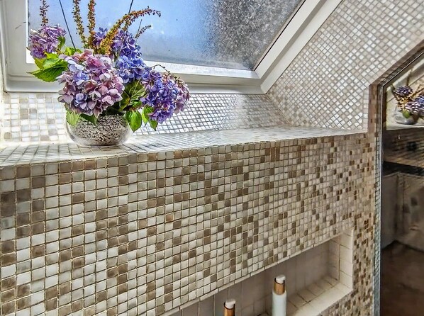 A bathroom with a tiled backsplash and a window with a flower arrangement.