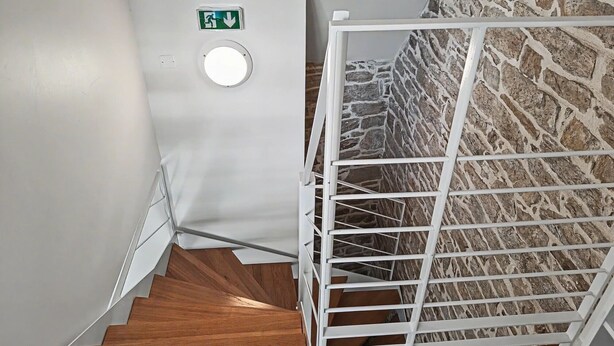 Una escalera con barandilla blanca, pasamanos de madera y pared de piedra.