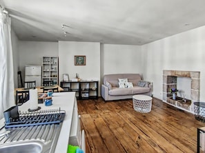 A modern living room with a sofa, a dining area with a table and chairs, a kitchen area with a sink and utensils, and a fireplace. - Charming two-story apartment in the heart of Pont-Aven (Pont-Aven)