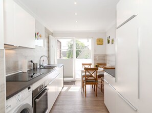 A modern kitchen with a built-in oven, a washing machine, and a dining area with wooden chairs. - Käpt n Stuv: Your cozy family vacation home near the beach in Büsum (Büsum)