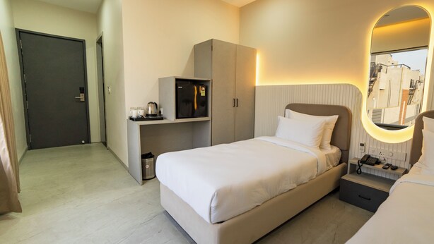 A hotel room with a bed, bedside table, a mirror, a wardrobe, and a kitchenette area. - Hotel Pinaki Inn (Ujjain)