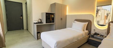 Habitación de hotel con cama, mesita de noche, espejo, armario y una pequeña cocina.