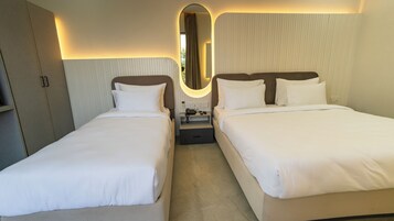 A hotel room with two single beds, a bedside table with a phone, and a mirror.