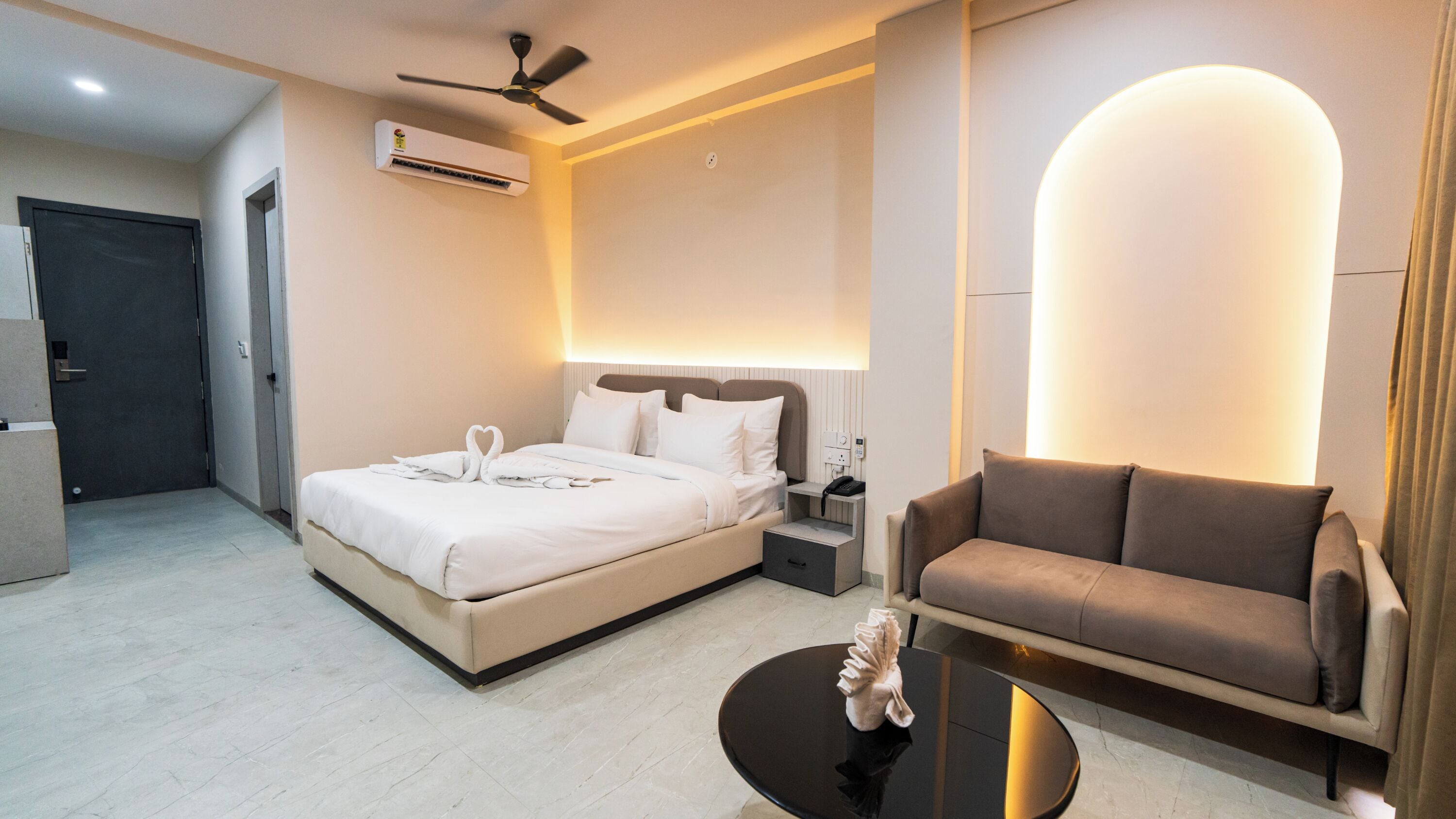 Une chambre d’hôtel comprenant un lit, un canapé, une table, un climatiseur, un ventilateur de plafond et un luminaire fixé au mur.