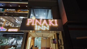 A hotel entrance with a prominent neon sign for 'PINAKI INN' and adjacent shops including 'Artize' and 'Noble Sanitation'. - Hotel Pinaki Inn (Ujjain)